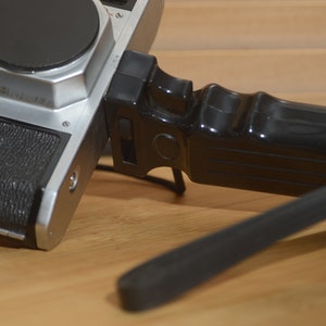 May include: A black and silver camera with a black hand grip attached. The camera has a black lens cap and the words "Asahi Pentax" written on the top.
