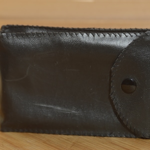 May include: A black leather case with a flap and a button closure. The case has a stitched edge and a smooth surface.
