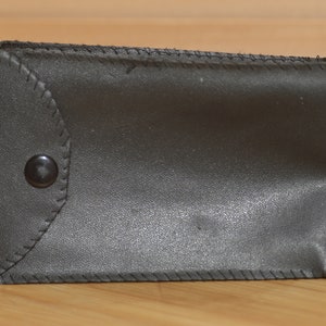May include: A black leather case with a flap and a snap closure. The case has a stitched design and a smooth finish.