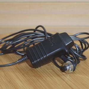 May include: A black electrical adapter with a coiled black cord and a silver connector. The adapter has the text "POWER SUPPLY" printed on it.