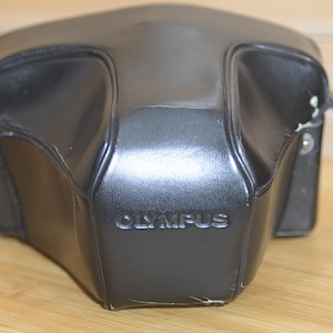 May include: Black leather camera case with the word "OLYMPUS" embossed on the front.