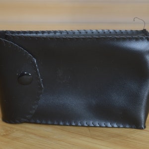 May include: A black leather case with a button closure. The case is stitched around the edges.