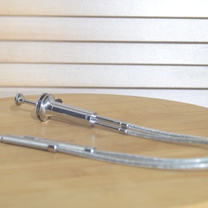 May include: A silver-toned plumbing tool with a long, flexible hose. The tool has a handle with a knob and a pointed tip.