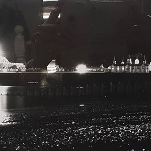 May include: A black and white photo of a pier at night with lights reflecting in the water.