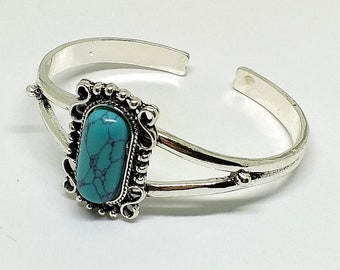 May include: A silver bangle bracelet with a turquoise stone set in a silver frame. The bracelet has a simple design and is perfect for everyday wear.