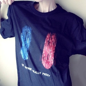 May include: A black t-shirt with a graphic of two blue and red streaks of light. The text "Is anyone really free?" is printed below the graphic.