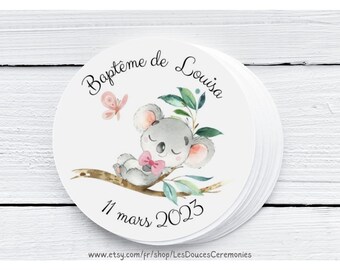 May include: Round sticker with a watercolor illustration of a koala bear sleeping on a branch with green leaves. The sticker says "Bapteme de Louisa" and "11 mars 2023".