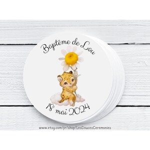 Op de afbeelding: Een stapel witte, ronde stickers met een aquarel illustratie. Het ontwerp toont een cartoon luipaardjong dat een madeliefje vasthoudt, met de tekst "Baptême de Lou" en "18 mai 2024".