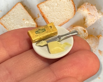 May include: A small white plate with a silver butter knife, a stick of butter, and a small amount of butter spread on the plate. The plate is being held by a hand.