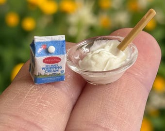 May include: A miniature carton of whipping cream next to a small glass bowl filled with whipped cream and a wooden spoon.