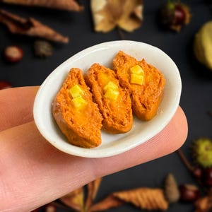 May include: Three miniature pieces of French toast on a white oval plate. The French toast is a light orange color and has a crispy texture. The French toast is topped with small squares of yellow butter.