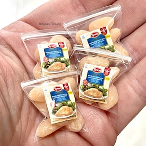 Puede incluir: Cuatro bolsas de plástico en miniatura llenas de pechugas de pollo en miniatura. Cada bolsa tiene una etiqueta de Tyson que dice "Tyson, Asadas y Listas, Pechugas de Pollo Sin Hueso Ni Piel".