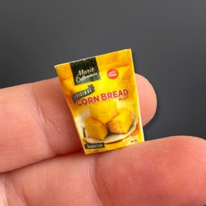 Puede incluir: Un paquete en miniatura de Marie Callender's Original Corn Bread Mix. El paquete amarillo presenta el nombre de la marca e imágenes de cuadrados de pan de maíz dorados. El texto "Corn Bread Mix" es claramente visible.