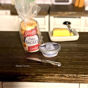 May include: A miniature kitchen scene with a bag of Sara Lee Everything Bagels, a small container of Philadelphia Cream Cheese, a small dish of butter, and a silver butter knife.