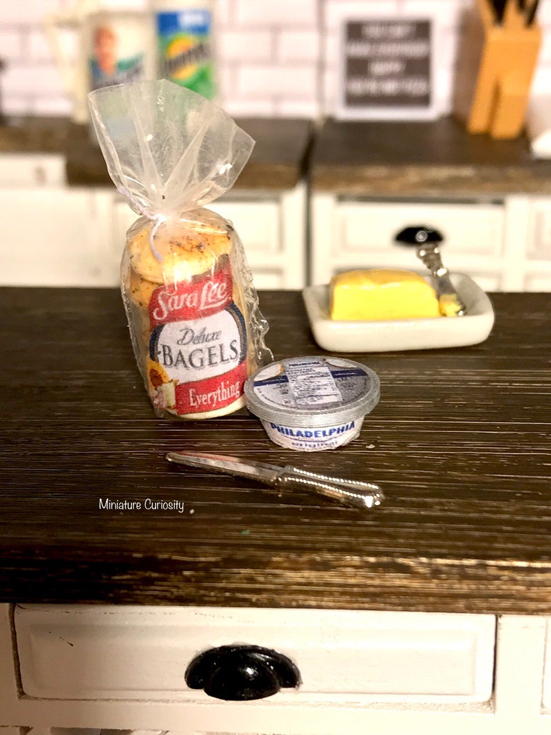 May include: A miniature kitchen scene with a bag of Sara Lee Everything Bagels, a small container of Philadelphia Cream Cheese, a small dish of butter, and a silver butter knife.
