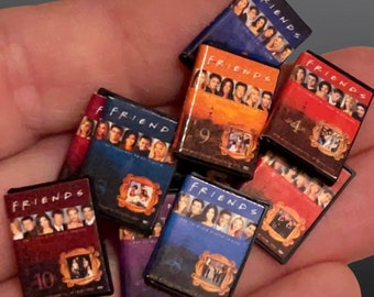 May include: A collection of ten DVD cases for the TV show "Friends". The cases are arranged in a pile, with the covers facing up. The covers are all different colors, with the show's logo and the season number printed on each one.