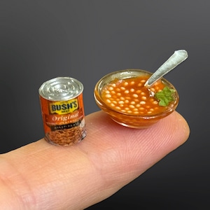 Peut inclure: Une boîte miniature de haricots cuits au four Bush's Original à côté d'un bol miniature de haricots blancs dans une sauce tomate avec une cuillère miniature.