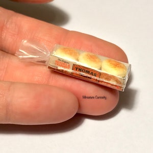 Könnte beinhalten: Eine Miniatur-Plastiktüte mit drei Miniatur-Thomas' English Muffins. Die Tüte befindet sich auf einer Hand. Die Verpackung ist orange und weiß mit dem Text "The Original" und "THOMAS' ENGLISH MUFFINS".