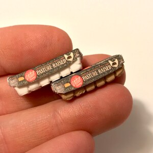 May include: Two miniature cardboard egg cartons with brown and white speckled designs. The cartons are labeled "Vital Farms Pasture Raised" in red and white text.