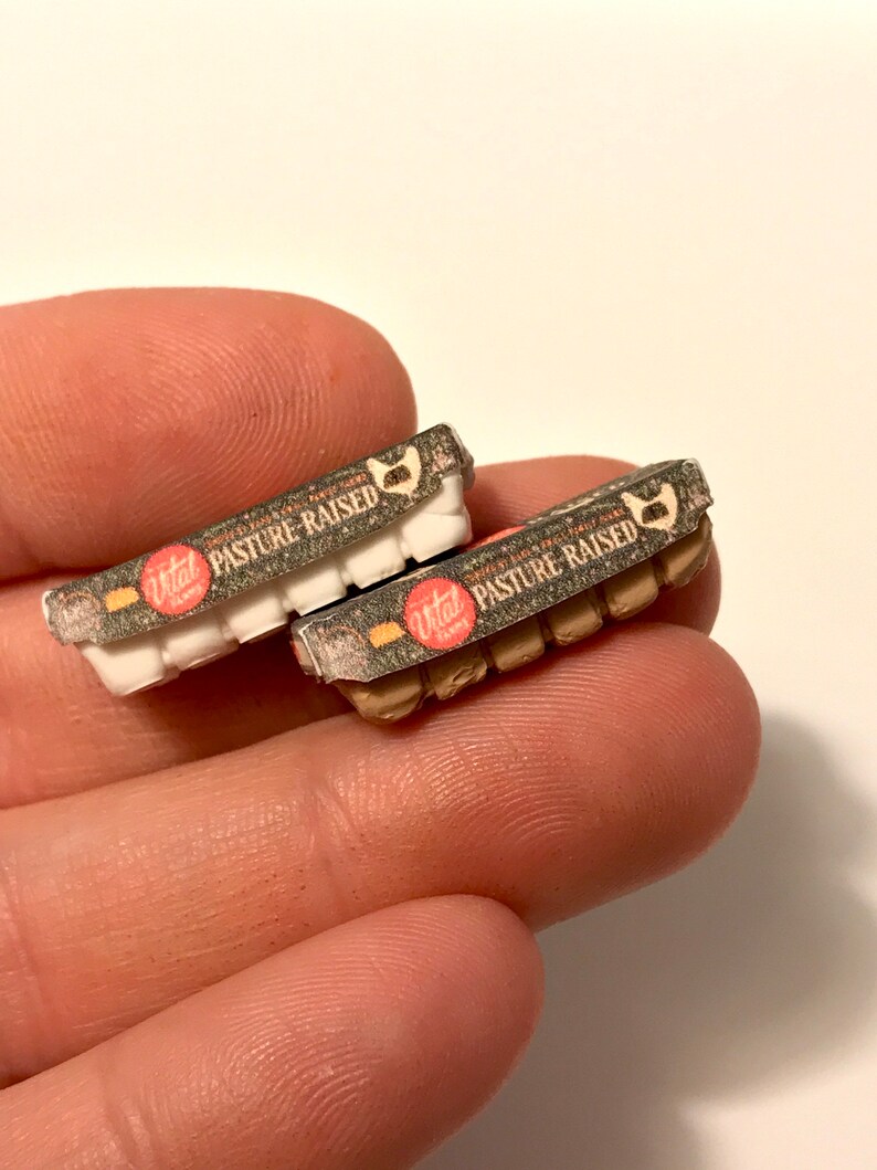 May include: Two miniature cardboard egg cartons with brown and white speckled designs. The cartons are labeled "Vital Farms Pasture Raised" in red and white text.