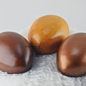 May include: Three wooden eggs, one brown, one dark brown, and one light brown. The eggs are smooth and polished.