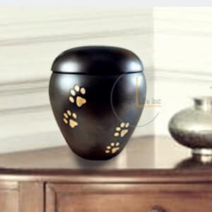 May include: Black ceramic pet urn with gold paw prints. The urn has a lid and is suitable for holding the ashes of a small pet.