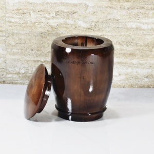 May include: A dark brown wooden urn with a lid. The urn has a smooth, polished finish and is made of solid wood. The lid is slightly ajar, revealing the interior of the urn.