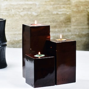 May include: Three wooden candle holders with lit tea lights. The holders are dark brown and stacked on top of each other. The candles are red, yellow, and green.