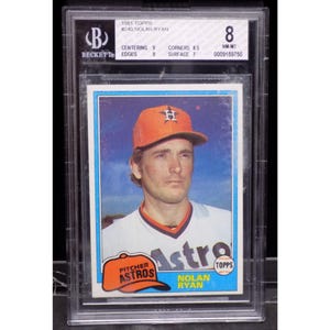 Könnte beinhalten: Eine Baseballkarte von Topps aus dem Jahr 1981 mit Nolan Ryan, Pitcher der Houston Astros. Die Karte ist von Beckett Grading Services mit NM-MT 8 bewertet. Die Karte zeigt ein Farbfoto von Ryan in seiner Astros-Uniform mit dem Teamlogo auf seiner Kappe. Die Karte enthält auch den Text "PITCHER ASTROS NOLAN RYAN TOPPS".