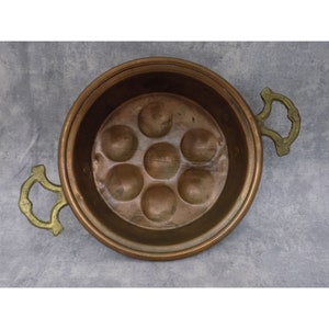 Puede incluir: Una sartén para pochar huevos de cobre con asas de latón. La sartén tiene siete hendiduras individuales para pochar huevos.