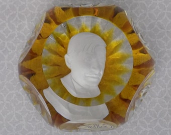 Può includere: Un fermacarte in vetro trasparente con un design giallo e bianco. Il fermacarte presenta un busto di una persona al centro. Il fermacarte ha il testo "Made in France" sul fondo.