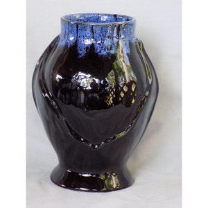 May include: Black ceramic vase with a blue glaze and a unique hand-shaped design.