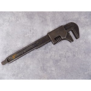 May include: A vintage adjustable wrench with a black metal finish. The wrench has a serrated jaw and a threaded adjustment mechanism.