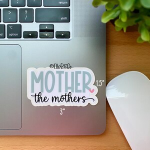 May include: A white sticker with the text "MOTHER the mothers" in blue and black lettering. The sticker is 3 inches wide and 1.5 inches tall.