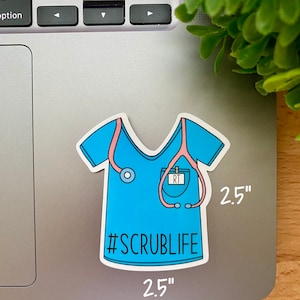 May include: A blue and pink 2.5 inch sticker of a medical scrub top with a stethoscope and name tag that says "RT". The sticker has the text "#SCRUBLIFE" on it.