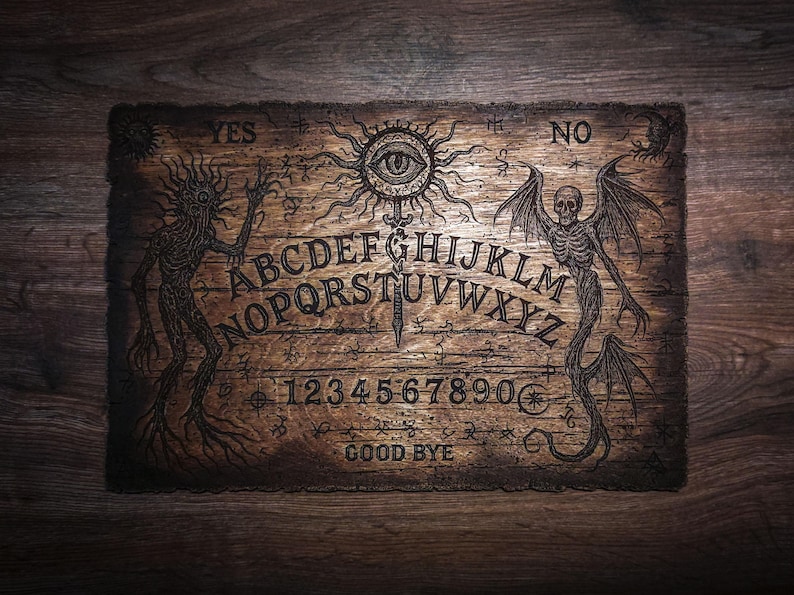 May include: A rectangular wooden spirit board featuring an engraved alphabet from A to Z, numbers 0 through 9, and the words YES, NO, and GOOD BYE. The board displays intricate illustrations of a central eye, a skeletal figure, and a creature.