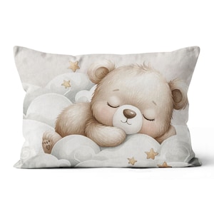 May include: A soft, white pillow with a brown teddy bear sleeping on a cloud. The bear has closed eyes and a cute, sleepy expression. The pillow is decorated with gold stars.