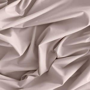 Könnte beinhalten: Nahaufnahme eines Stoffes mit weichen Falten. Der Stoff hat eine einfarbige, gedämpfte rosa Farbe. Das Bild zeigt die Textur und den Fall des Materials, wobei Schatten den Falten Tiefe verleihen. Der Stoff scheint glatt zu sein und möglicherweise eine Baumwoll- oder Leinenmischung.