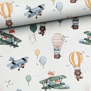 Può includere: Un tessuto chiaro con un motivo ripetuto di illustrazioni fantasiose. Il design include aerei, mongolfiere e vari animali come orsi, volpi e procioni. Gli animali sono raffigurati in aria con palloncini. Il tema generale è giocoso e adatto agli articoli per bambini.