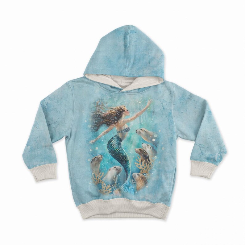 May include: A light blue hoodie featuring a mermaid design. The illustration shows a mermaid with flowing brown hair and a teal tail, surrounded by seals. The hoodie has a light blue hood and cuffs, with a cream-colored lining.