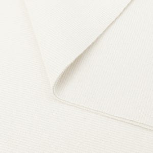 May include: Close-up of a folded, off-white knit fabric. The fabric has a ribbed texture, with visible horizontal lines. The edge of the fabric is curved, revealing the inside. The overall appearance is clean and simple.