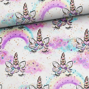 Puede incluir: Una tela blanca con un patrón repetido de caras de unicornio con los ojos cerrados y arcos de arcoíris. Los unicornios tienen cuernos dorados y corazones rosas en la frente. El fondo es blanco con un efecto acuarela rosa claro y azul y purpurina dorada.