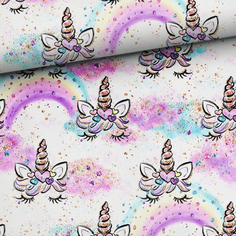 May include: A white fabric with a repeating pattern of unicorn faces with closed eyes and rainbow arches. The unicorns have gold horns and pink hearts on their foreheads. The background is white with a light pink and blue watercolour effect and gold glitter.