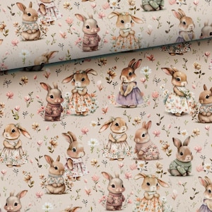 May include: Beige fabric with a repeating pattern of cartoon bunnies in dresses and sweaters. The bunnies are surrounded by small flowers and foliage in pink, brown, and green, creating a whimsical design.