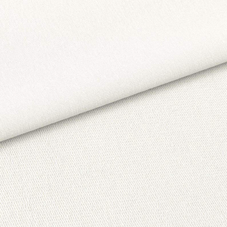 May include: Close-up of a white fabric with a textured surface. The fabric is folded diagonally, revealing a smooth, ribbed texture on one side and a more textured, slightly bumpy surface on the other. The color is a bright, clean white.