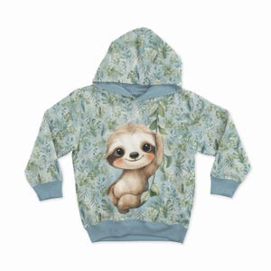 Puede incluir: Una sudadera con capucha de color azul claro con un estampado de hojas tropicales y helechos verdes. En el centro, una ilustración detallada de un perezoso marrón colgado de una enredadera verde, con mangas largas y puños lisos.