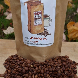 May include: A brown paper bag with a label that says "Jack & the Bean" and "Koffee Blends". The label also says "Origin: Nicaragua" and "Roast: Light". The bag is filled with coffee beans.