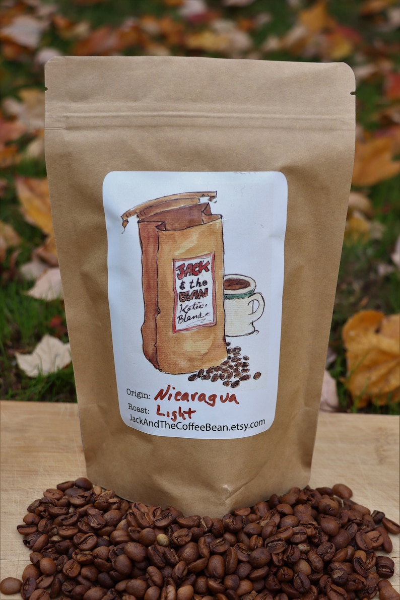 May include: A brown paper bag with a label that says "Jack & the Bean" and "Koffee Blends". The label also says "Origin: Nicaragua" and "Roast: Light". The bag is filled with coffee beans.