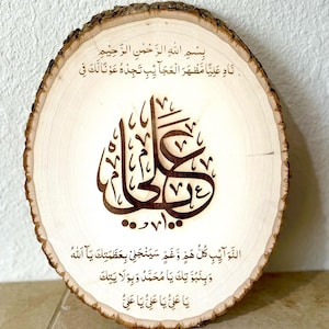 May include: A wooden round slice with a brown wood grain pattern. The slice has an inscription in Arabic script, which reads "Bismillah ir-Rahman ir-Rahim Nad Aliya Mazhara al-Ajaib Tajede Awna Laka Fi al-Nawaib Kullu Haza Wa Gham Sayanjalli Bi-Azamatik Ya Allah Wa Binubuwwatik Ya Muhammad Wa Bi-Wilayatik Ya Ali Ya Ali Ya Ali".