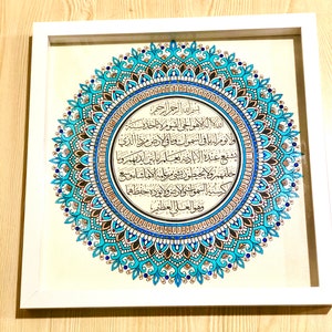 May include: A framed artwork featuring a blue and gold mandala with Arabic calligraphy. The calligraphy reads "Bismillah ir-Rahman ir-Rahim" and continues with a passage from the Quran.